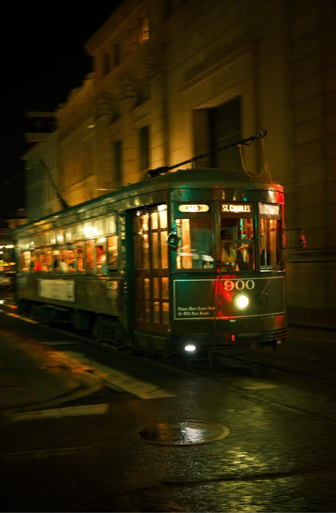 Green streetcar number 900 glowing at night on a wet street beside lit building facades, New Orleans.