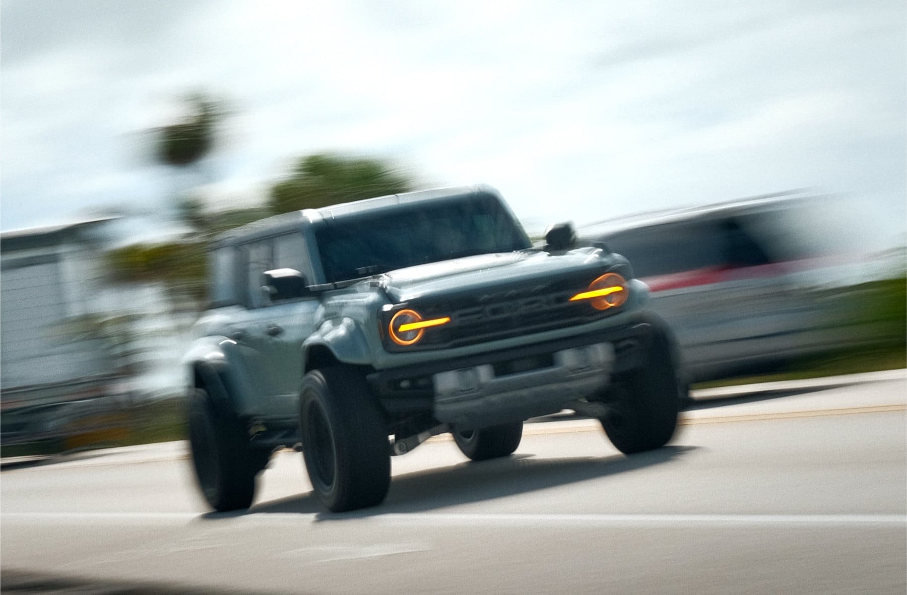 Panned shot of a dark gray off-road truck with amber headlights, sharp against a streaked, blurred street.