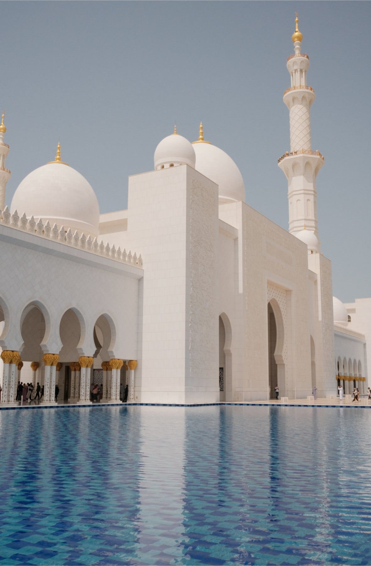 White domes, arches and a gold-tipped minaret of a grand mosque rising above a blue reflecting pool.