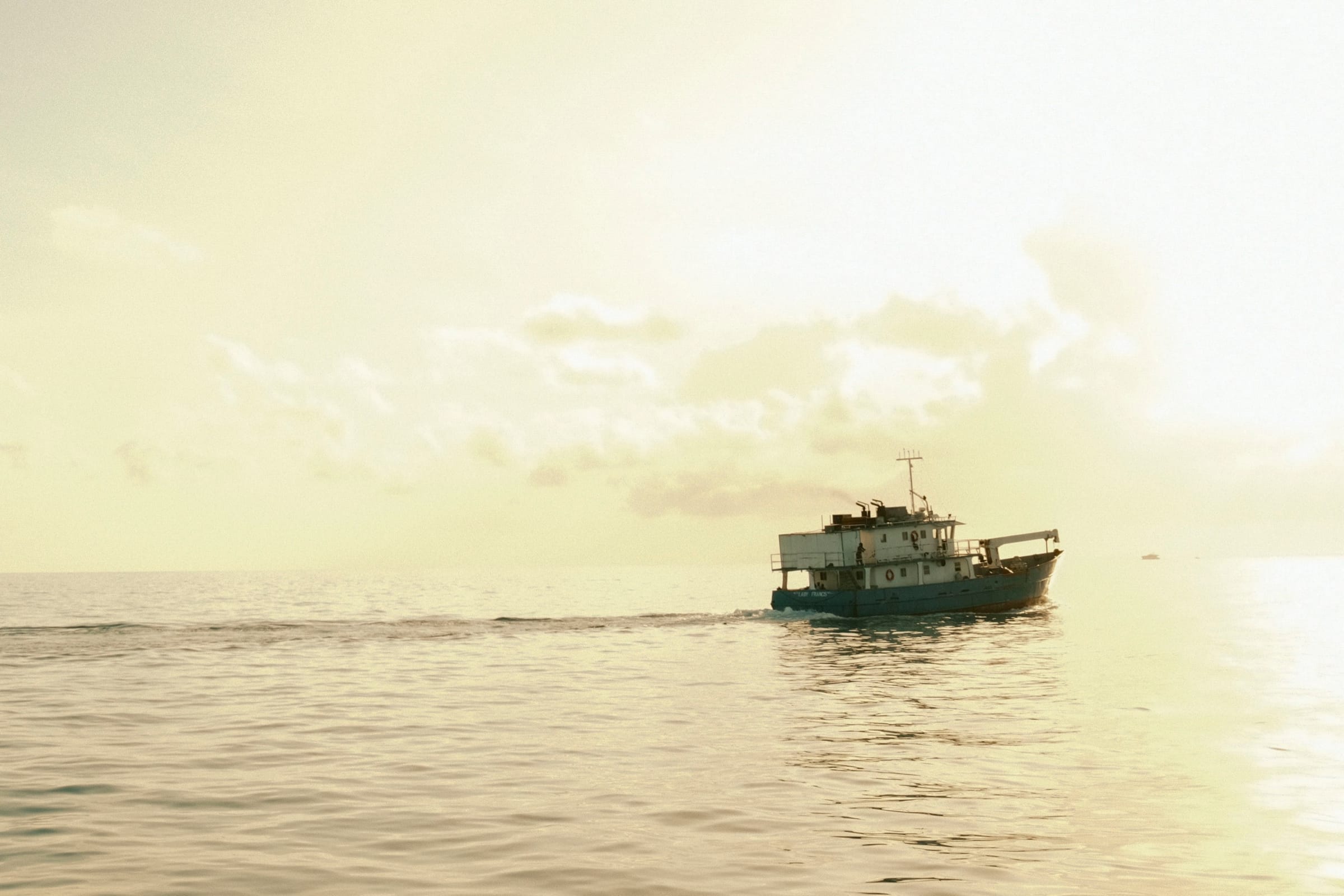 Work boat on the sea against hazy sunlight that washes the sky and water in pale yellow.