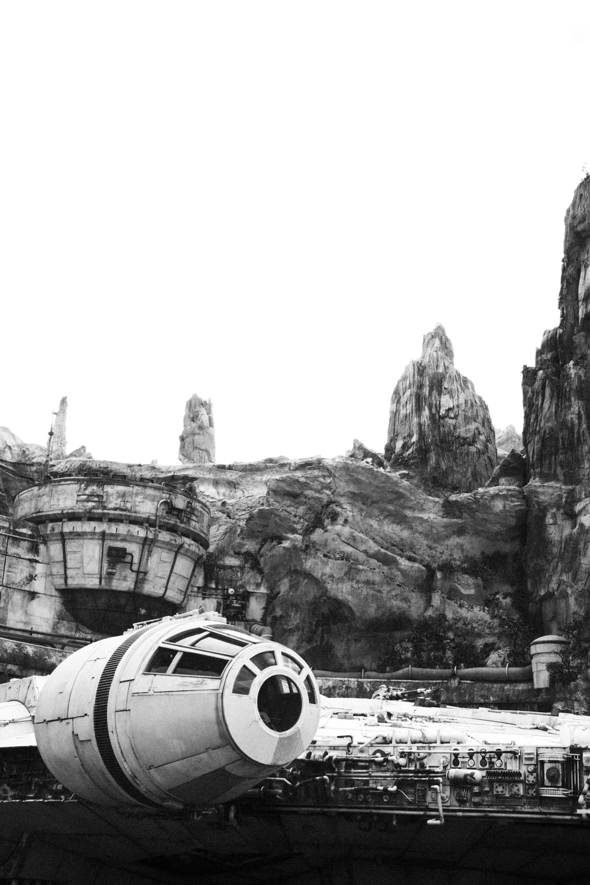 Black-and-white photo of a full-size Millennium Falcon replica beneath towering rock spires at a theme park.