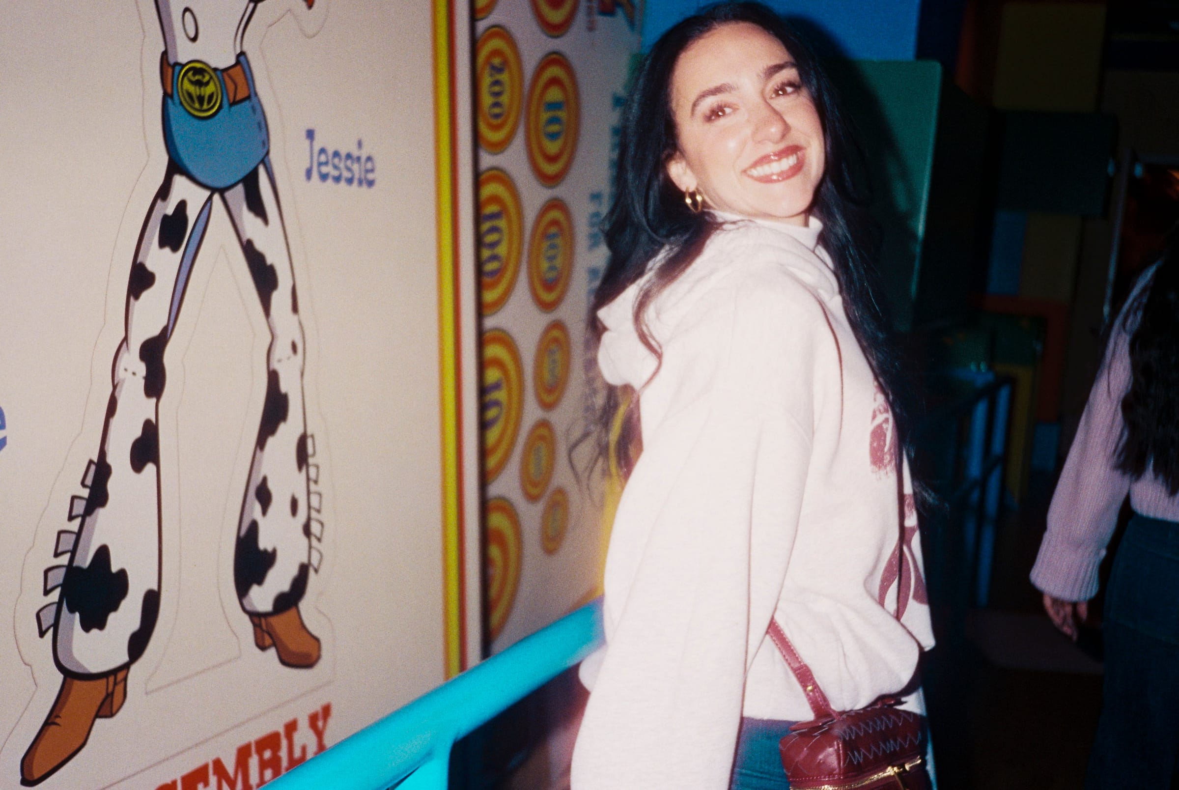 Flash photo of a smiling woman in a white hoodie beside a Toy Story Jessie cutout with cow-print chaps.