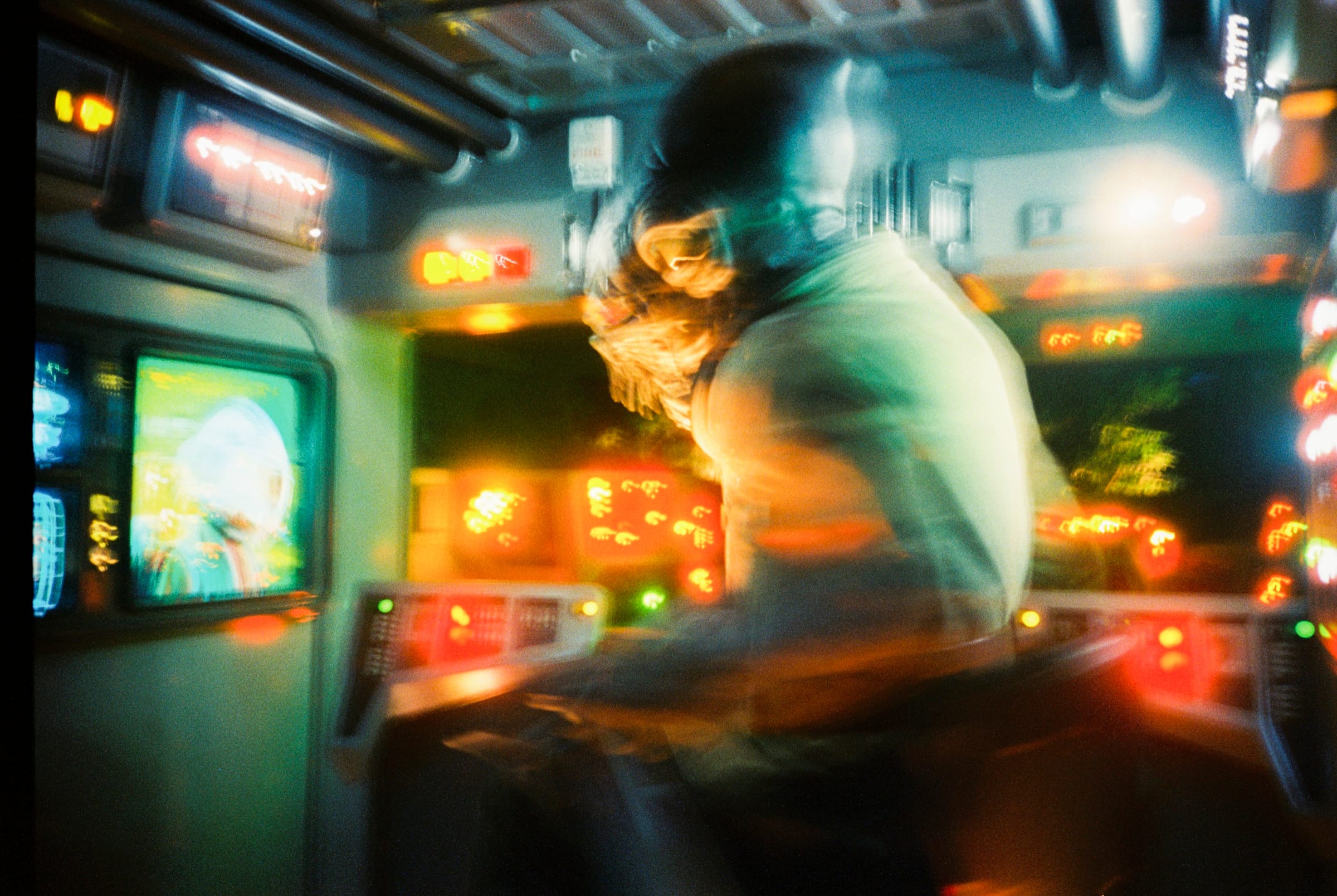 Motion-blurred interior of a ride cockpit, with glowing screens and red and amber lights around a seated figure.