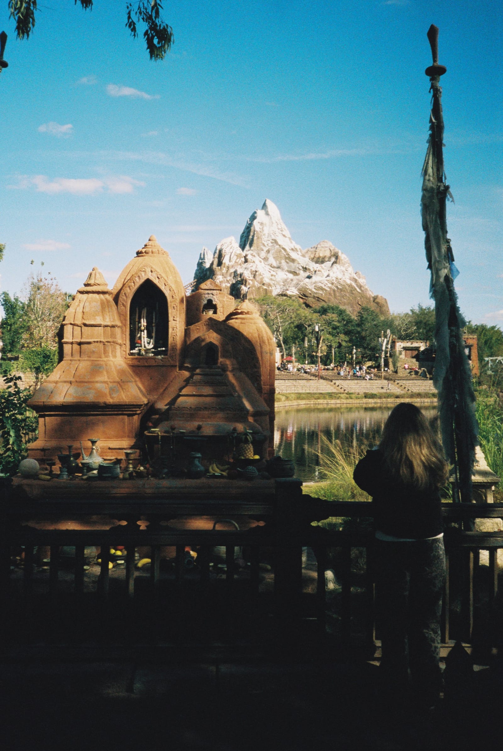 Film photo of a carved temple facade and a snowy mountain peak under blue sky, with a woman in silhouette.