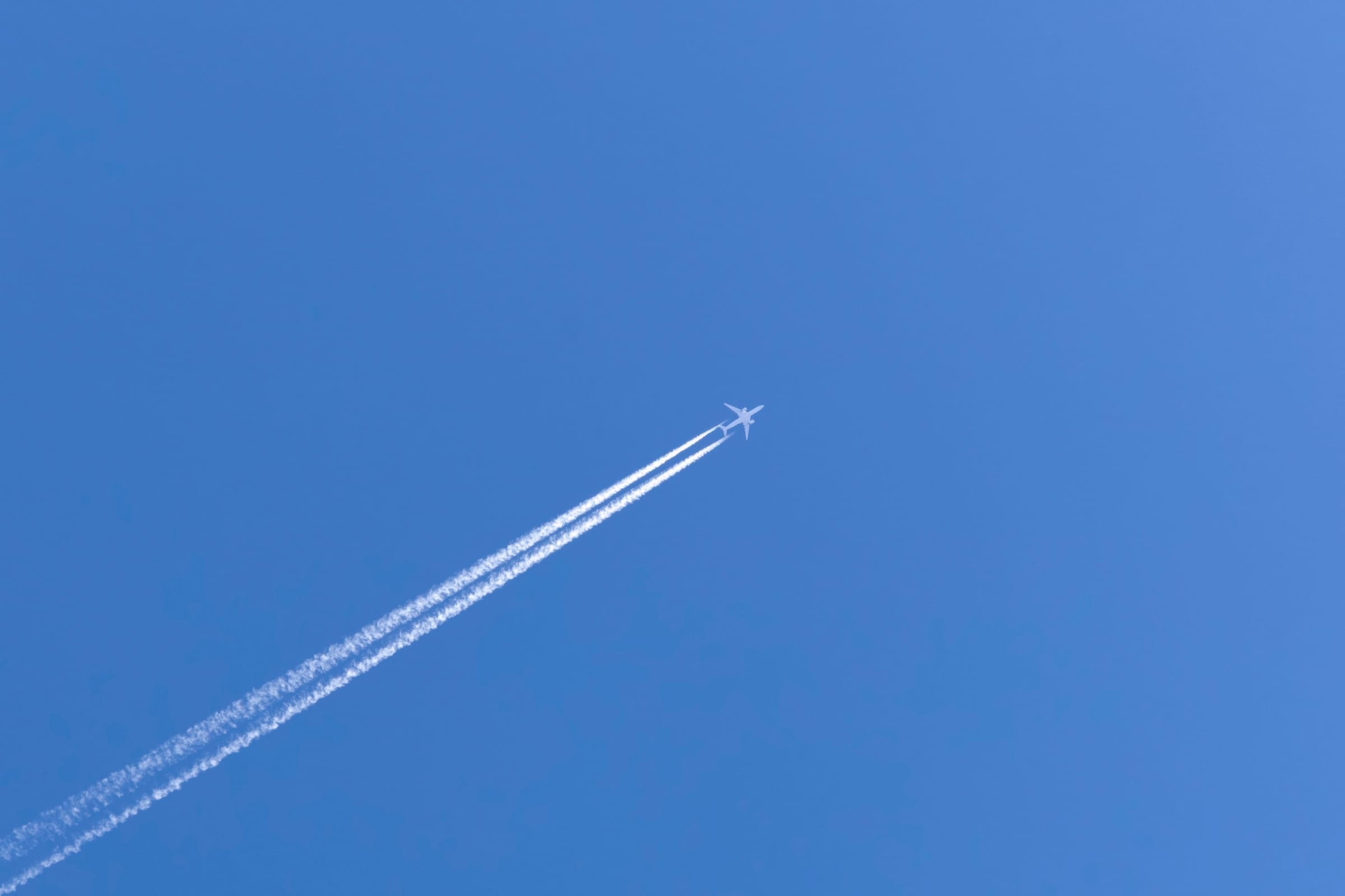 Jet plane crossing a deep blue sky, trailing twin white contrails diagonally across the frame.