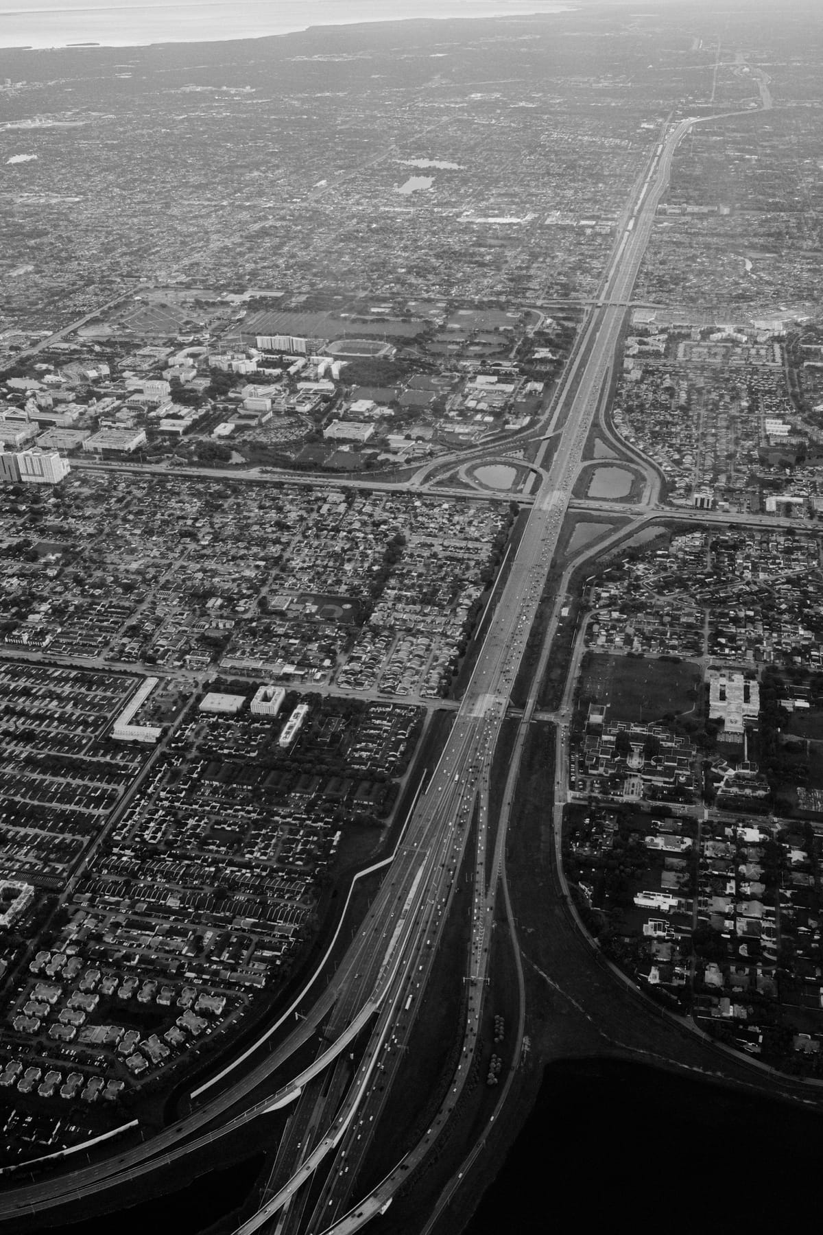 Black-and-white aerial view of a highway cutting through a dense city grid toward a hazy coastline.